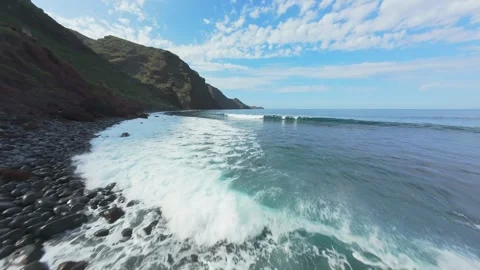 Powerful waves crash against volcanic rocky shore, surfers riding swells along 스톡 동영상 308588752