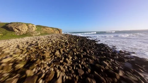 Powerful waves tumble over jagged rocks near golden cliffs Video stock 346075601