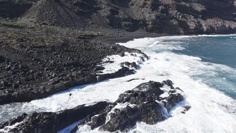 Powerful white waves breaking against dark volcanic shoreline, generating Stock Footage 308413637