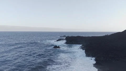 Powerful white waves breaking rhythmically against dark volcanic shoreline under 스톡 동영상 308402642