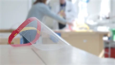 PPE face visor by a desk while people make more masks in the background Video stock 129823556