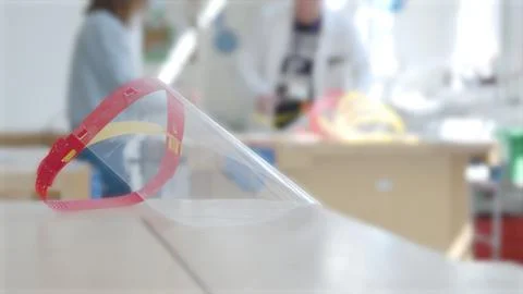  PPE face visor by a desk while people make more masks in the background Foto stock