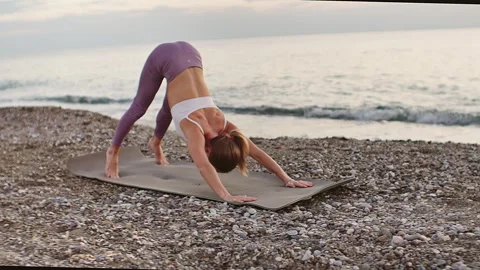 Practice yoga at sunset on a sandy beach by the sea. A woman performs gentle Stock Footage 303693173