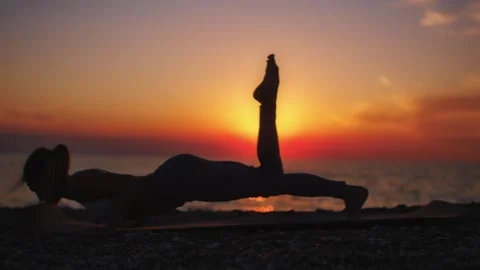 Practice yoga at sunset on a sandy beach by the sea. A woman performs gentle Stock Footage 303693289