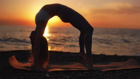 Practice yoga at sunset on a sandy beach by the sea. A woman performs gentle Stock Footage 303693403