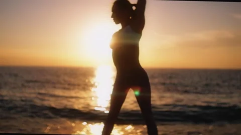 Practice yoga at sunset on a sandy beach by the sea. A woman performs gentle Stock Footage 303693408