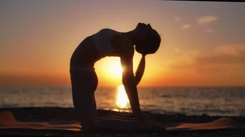 Practice yoga at sunset on a sandy beach by the sea. A woman performs gentle Stock Footage 303693650