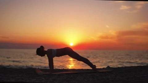Practice yoga at sunset on a sandy beach by the sea. A woman performs gentle Stock Footage 303693752