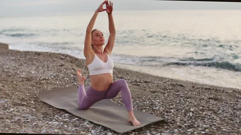 Practice yoga at sunset on a sandy beach by the sea. A woman performs gentle Stock Footage 303693765