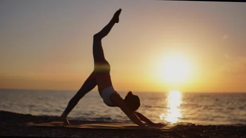 Practice yoga at sunset on a sandy beach by the sea. A woman performs gentle Stock Footage 303693793