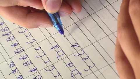 Practicing handwriting on lined paper with a blue pen in a study environment Stock Footage 345090106