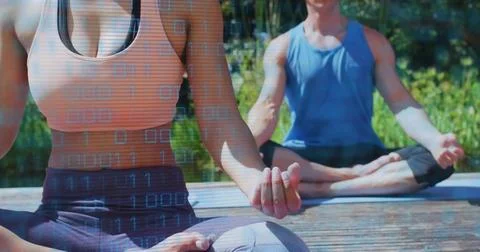 Practicing pair in orange crop and blue tank meditating on dock with yoga mats, 库存照片