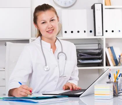 Practicioner female in uniform is working behind laptop with documents Stock Photos