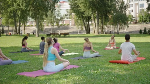 Practitioners doing head bends together with yoga instructor in sunny park Stock Footage 247699011