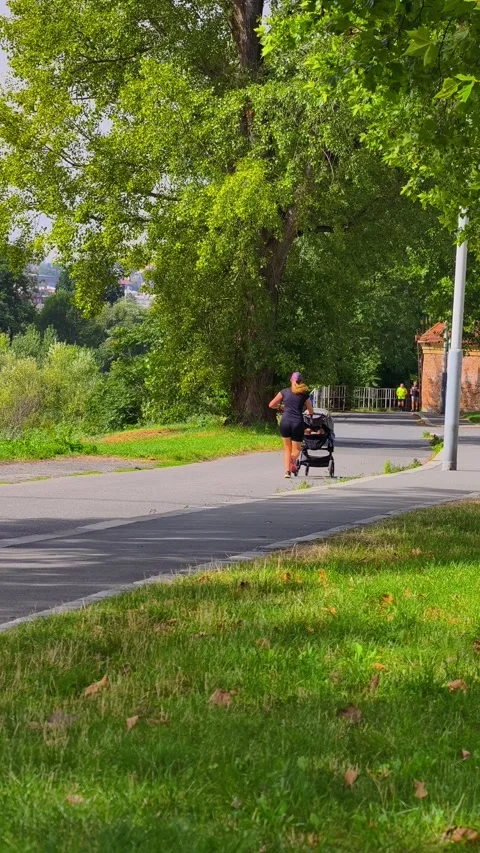 PRAGUE, CZECH REPUBLIC – AUGUST 28, 2026: Mother runs through a green park 스톡 동영상 343926371