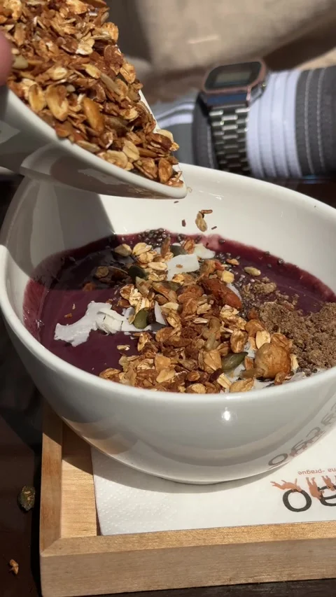 Prague, czech republic - may 11, 2026 - hand adds toasted granola cereal to a Stock Footage 334951432