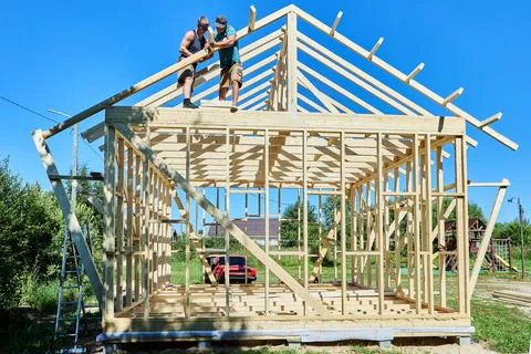 Pratt Truss roof framework under construction as two workers position rafte.. Stock Photos