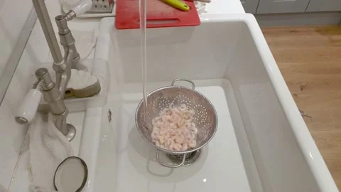 Prawns or shrimp defrosting under a tap in a strainer, in a kitchen sink Stock Footage 148269229