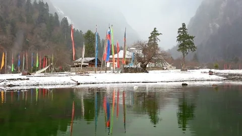 Prayer flags reflected in a lake in snowy tibet on an overcast day Stock Footage 312303417