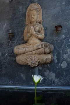 Praying buddha statue on stone wall above white water lily flower Stock Photos