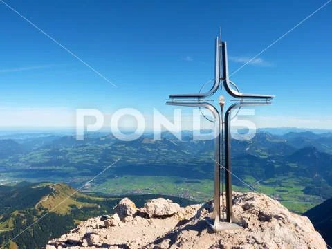 Praying cross raised at mountain summit in Alps. Sharp peak, daybreak Sun in Stock Photos