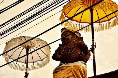 Praying stone statue between two umbrellas on the roof of the temple in Ubud. Stock Photos