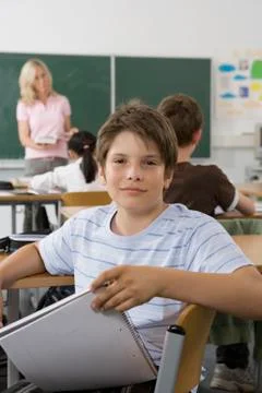 A pre-adolescent boy sitting in the back of a classroom, looking at camera Stock Photos