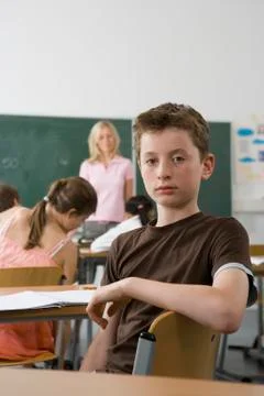 A pre-adolescent boy sitting in the back of a classroom, looking at camera Stock Photos