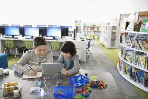 Pre-adolescent boys programming electronics at digital tablet in library Foto stock