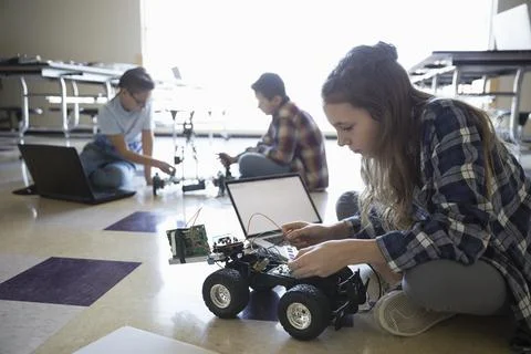 Pre-adolescent girl programming robotics at laptop on classroom floor 스톡 사진
