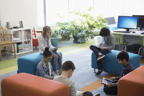 Pre-adolescent students reading with digital tablets in library Stock Photos