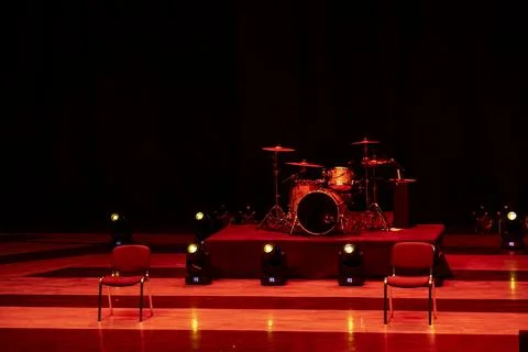 A pre-performance scene in red light with a drum set in the middle Stock Photos