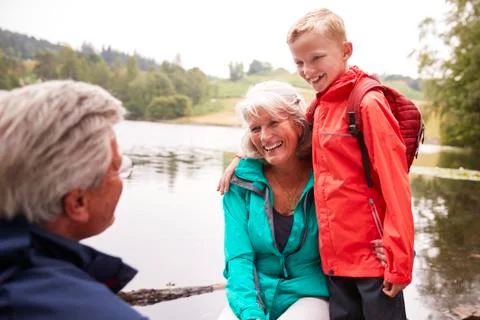 Pre-teen boy standing beside his grandparents, sitting on the shore of a lake Stock Photos