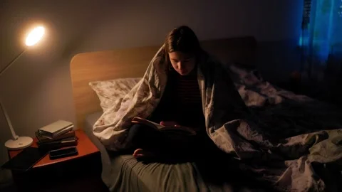 Preadolescent focused on reading a textbook in bed by lamp light Stock-Footage 336669312