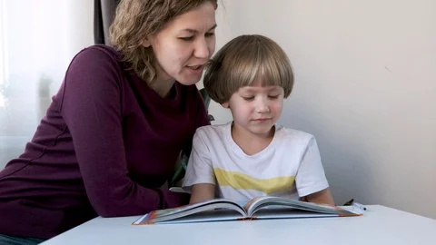 Prechool boy, child, sitting at the table at home and reading with his mom Stock Footage 124110237