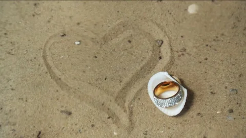 Precious ring in shell on sandy bottom, next to heart drawn in sand. Stock Footage 255364340