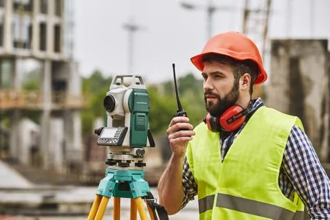 Precise measurements. Surveyor engineer in protective wear and red helmet using Stock Photos