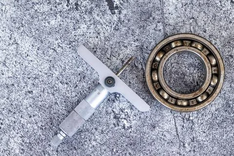 Precision depth micrometer gauge lying beside steel ball bearing on concret.. Stock Photos