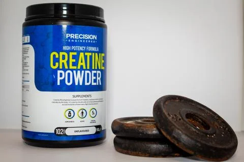 Precision Engineered creatine powder and a stack of metal weights against a p Stock Photos