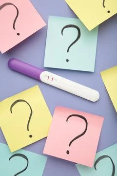 Pregnancy test with two stripes with question marks on purple background. Top Stock Photos