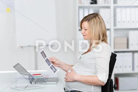 Pregnant businesswoman looking at ultrasound scan reports at desk Stock Photos