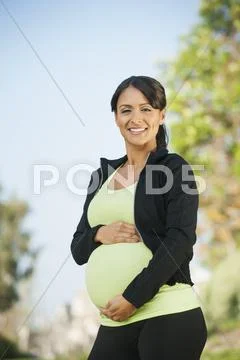 Pregnant Hispanic woman holding her belly outdoors Stock-Fotos