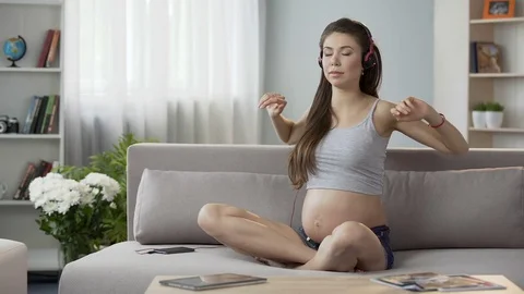 Pregnant lady sitting in headphones exercising, audio guide to pregnancy yoga Stock Footage