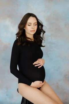 Pregnant model sitting on stool caressing her belly Stock Photos