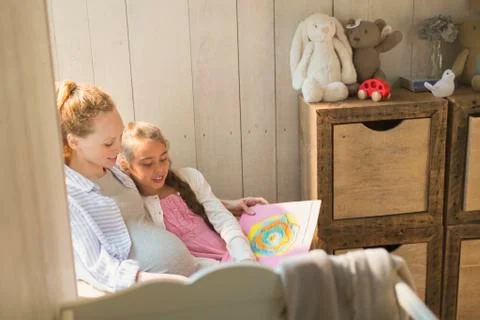 Pregnant mother and daughter reading story book in nursery Stock Photos