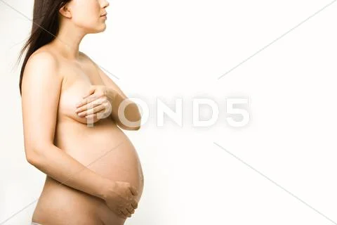 Pregnant nude woman standing in profile and touching her tummy Stock Photos