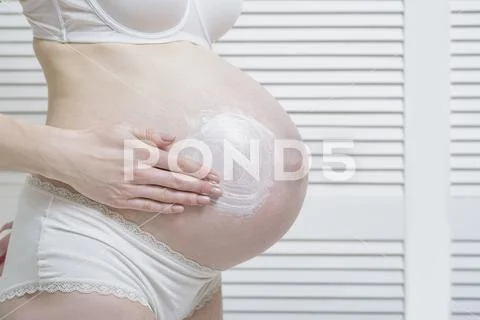 Pregnant woman applies cream on her belly. Close-up Stock Photos