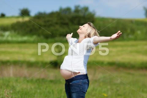 Pregnant woman with arms outstretched at field Stock-Fotos