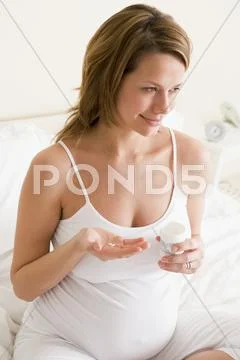 Pregnant woman in bedroom holding medicine and water smiling Stock-Fotos
