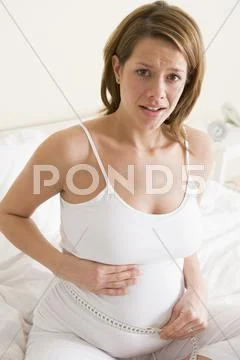 Pregnant woman in bedroom measuring belly looking worried Stock Photos